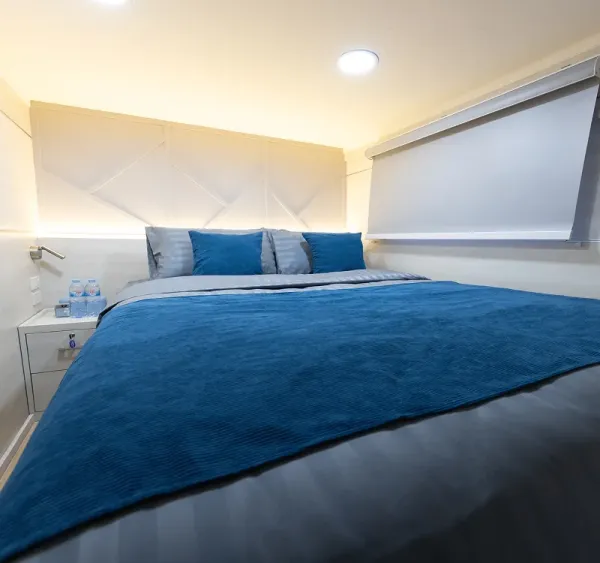 Deluxe cabin A1 on Krishna 3 — a double bed beside a window with a roller blind
