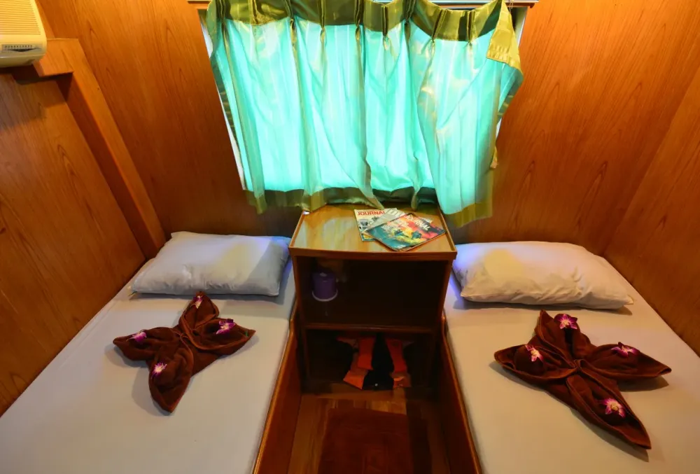 Twin cabin on Manta Queen 2 — bedside unit between the beds and a curtained window