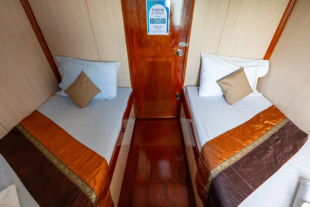 Made-up twin cabin on Manta Queen 2 with a bedside unit by the door