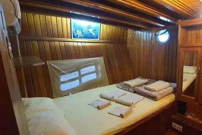 Timber-lined Okyanus JD cabin with a double bed, two portholes and a shelf above the headboard
