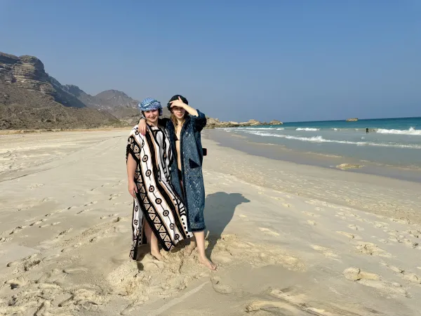 Two girls on a wild Dhofar beach — white sand, mountains, ocean