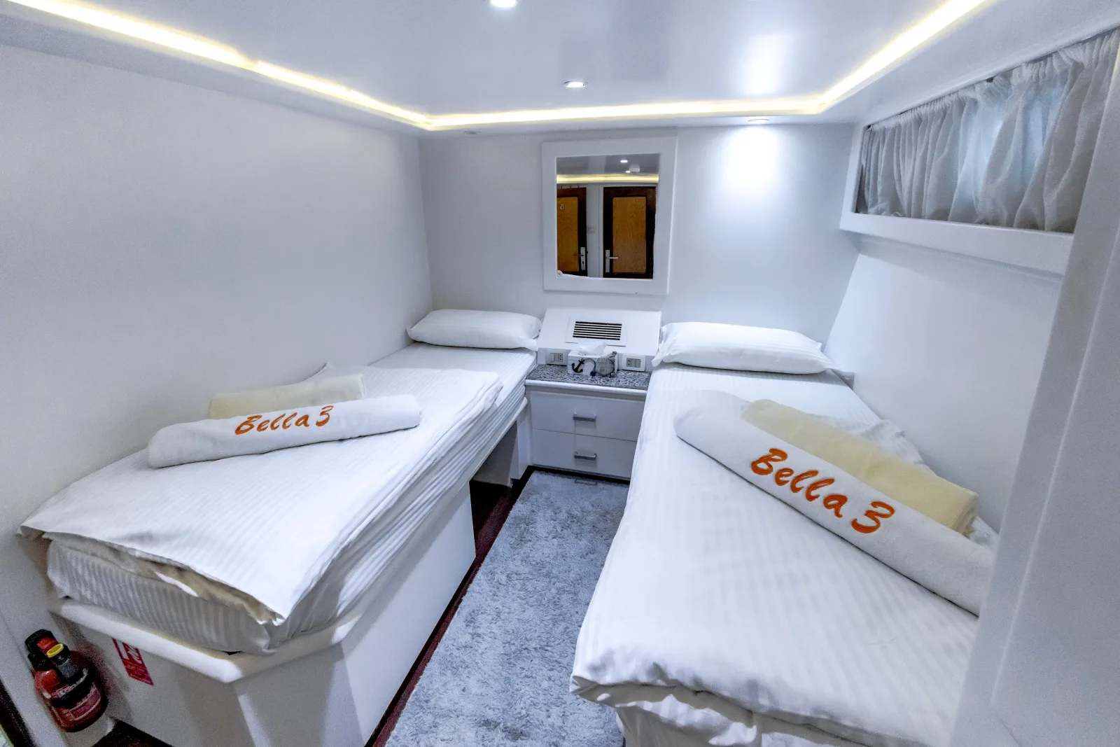 Bella 3 twin cabin — bedside unit between the beds and a bulkhead window