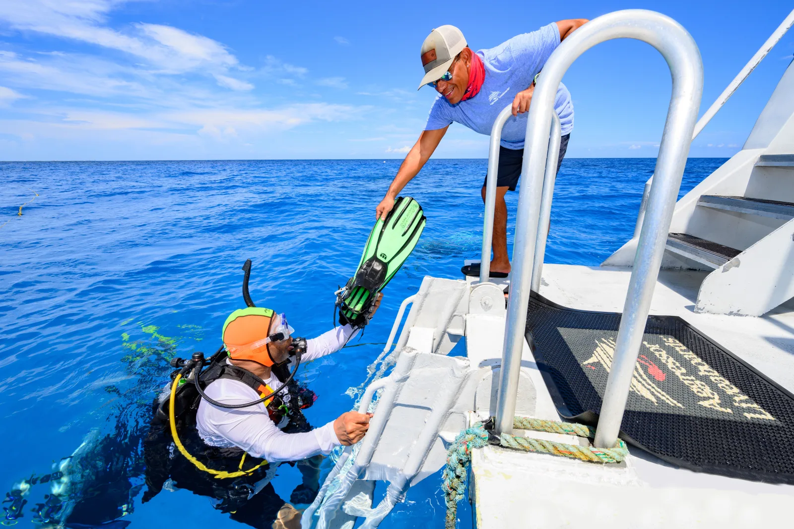 Crew member taking fins from a diver at the ladder of Cayman Aggressor IV