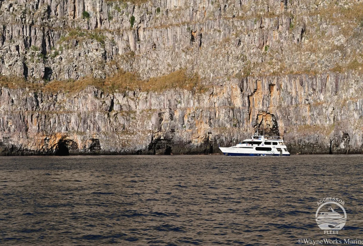 Galapagos Aggressor III at the foot of a cliff, seen from a distance