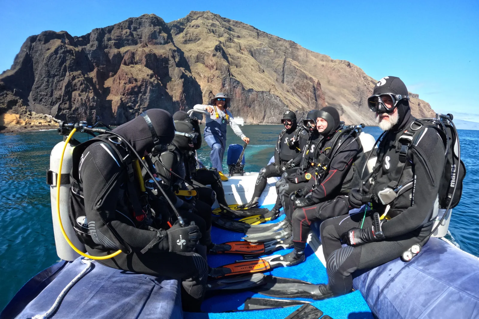Divers in a panga beside a rocky shore before the dive