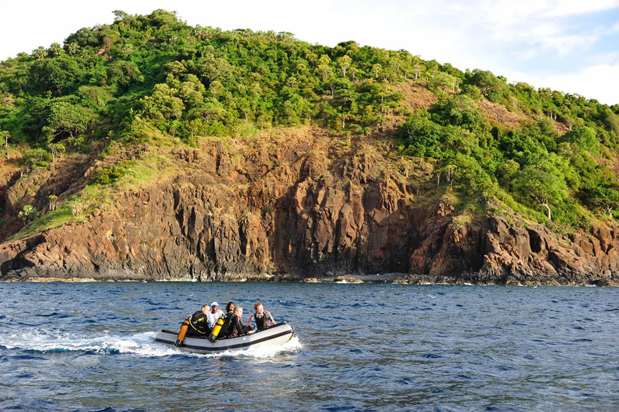 Divers heading for the site by tender along a rocky island