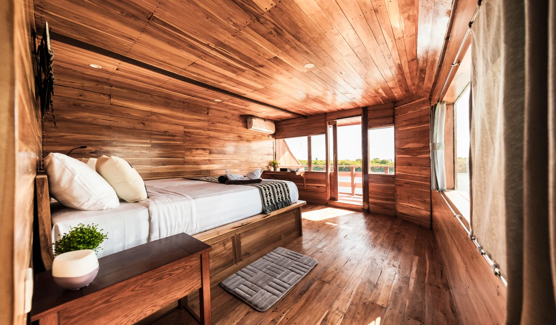 Upper-deck cabin on Komodo Aggressor — timber walls and ceiling and the door out to the private balcony