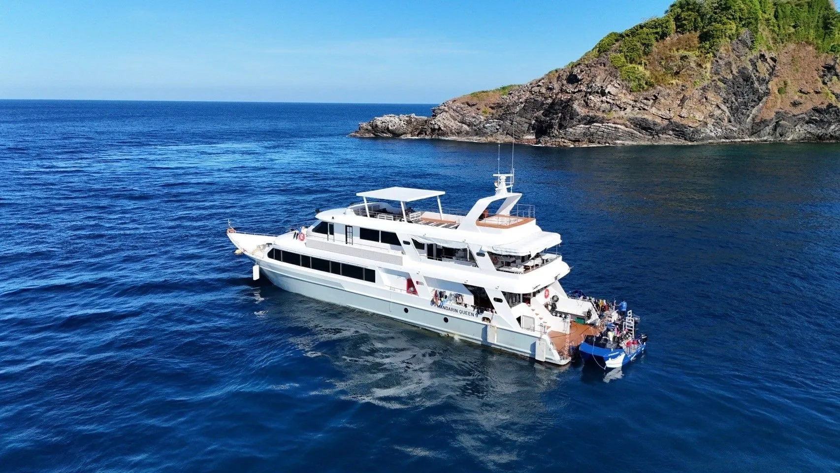 The vessel moored beneath a green island — drone view