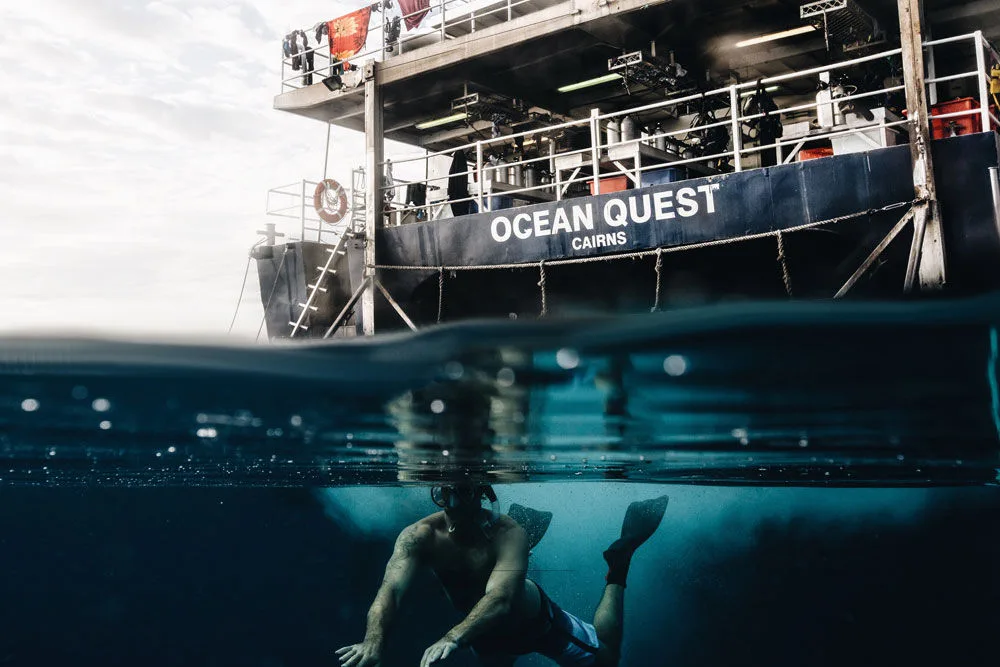 Swimmer under the hull lettered Ocean Quest Cairns, half-underwater shot