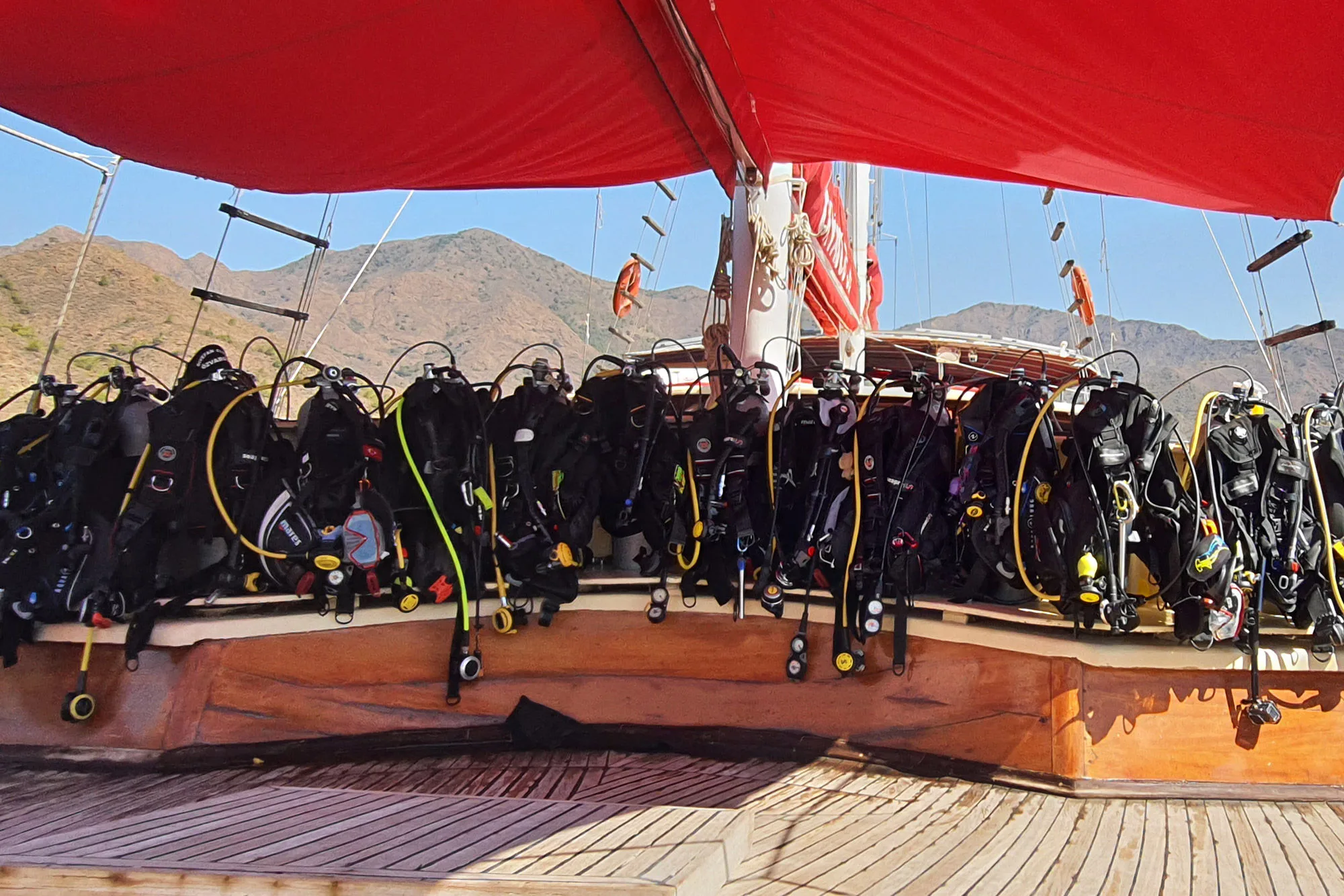 Rigged scuba kits lined up along the dive deck under the red awning