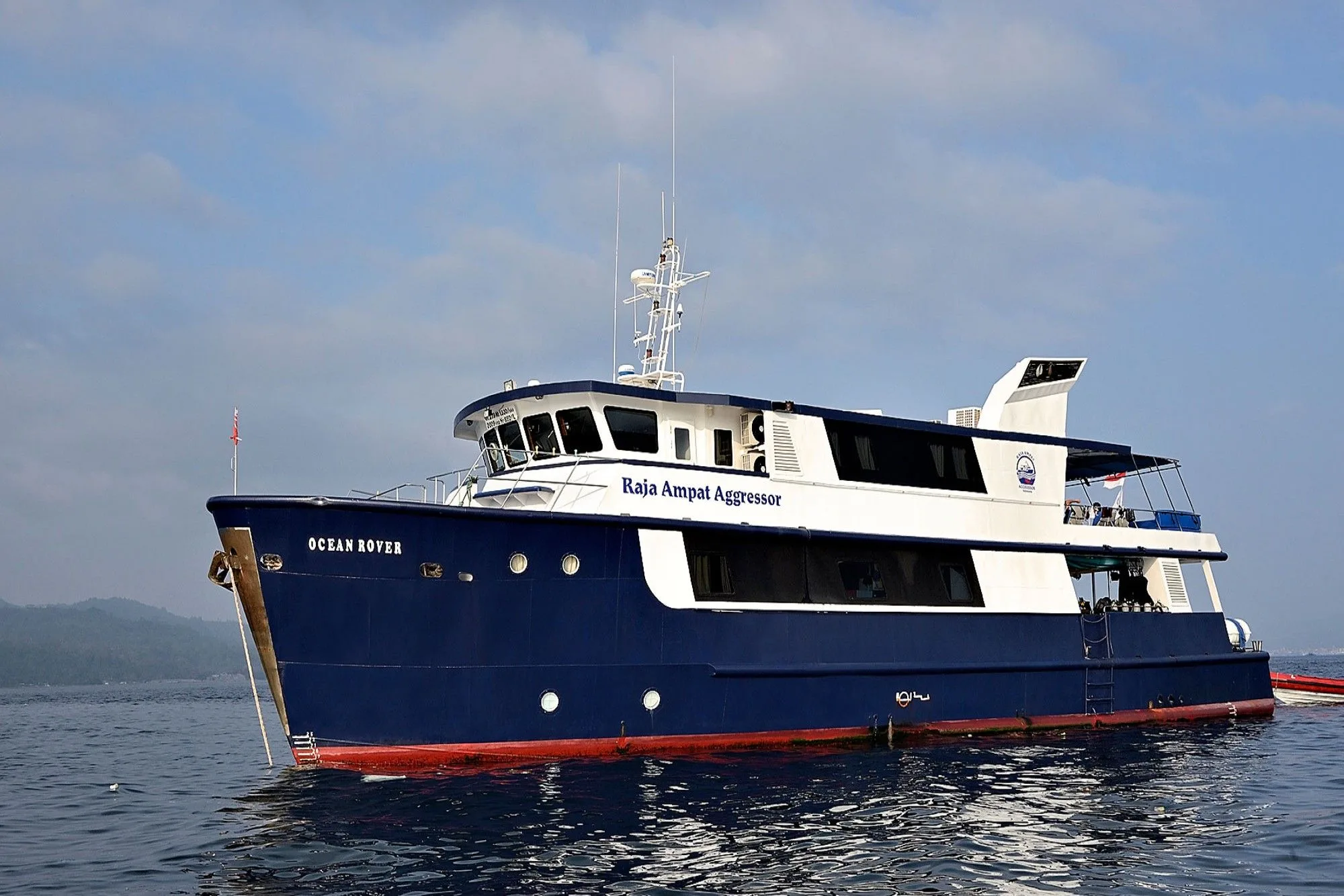 Raja Ampat Aggressor на якоре — стальной синий корпус с надписями OCEAN ROVER на скуле и Raja Ampat Aggressor по надстройке