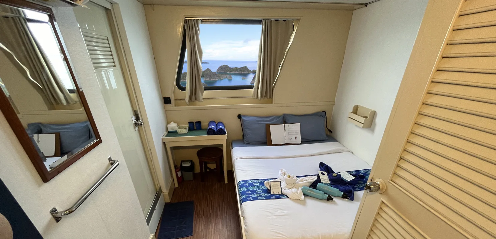 Master Stateroom верхней палубы Raja Ampat Aggressor — кровать queen у панорамного окна, зеркало с полкой и шкаф-жалюзи