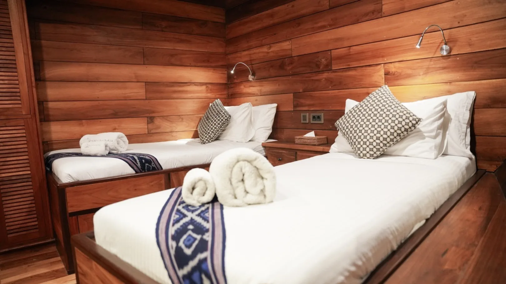 Twin beds under teak panelling with rolled towels and cushions