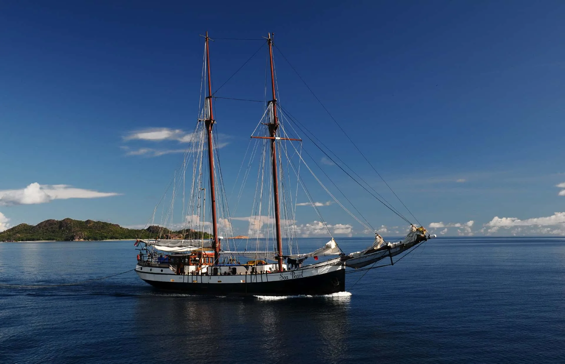Sea Pearl at anchor in deep blue water under her red masts