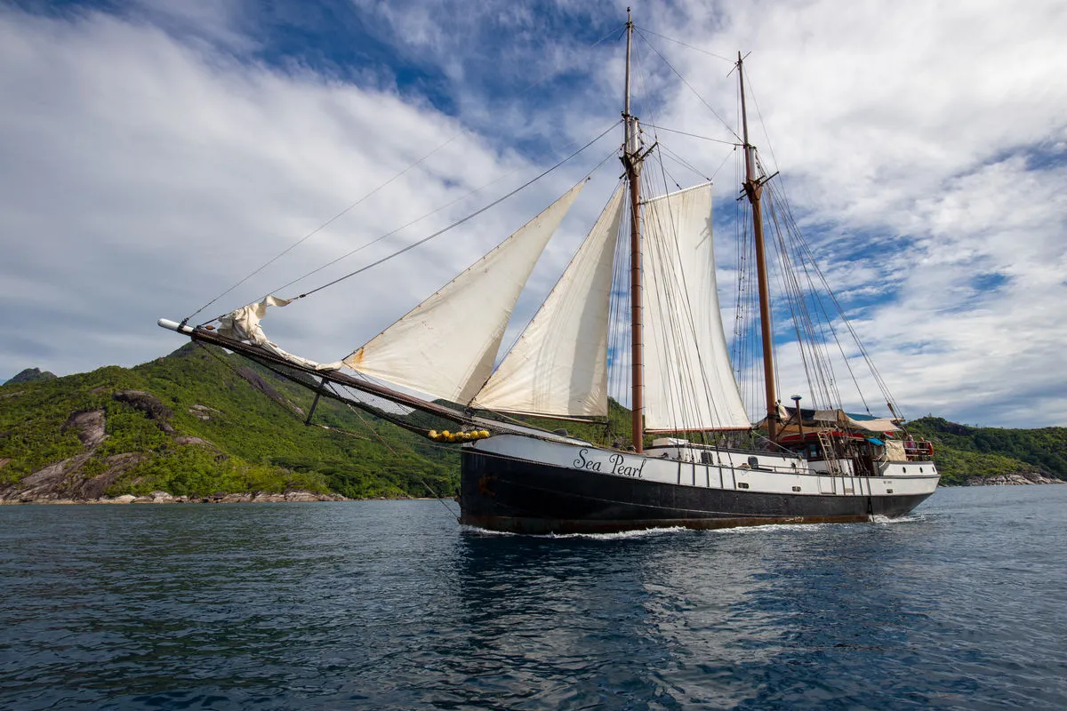 The black hull of Sea Pearl with her name on the topsides against a green island