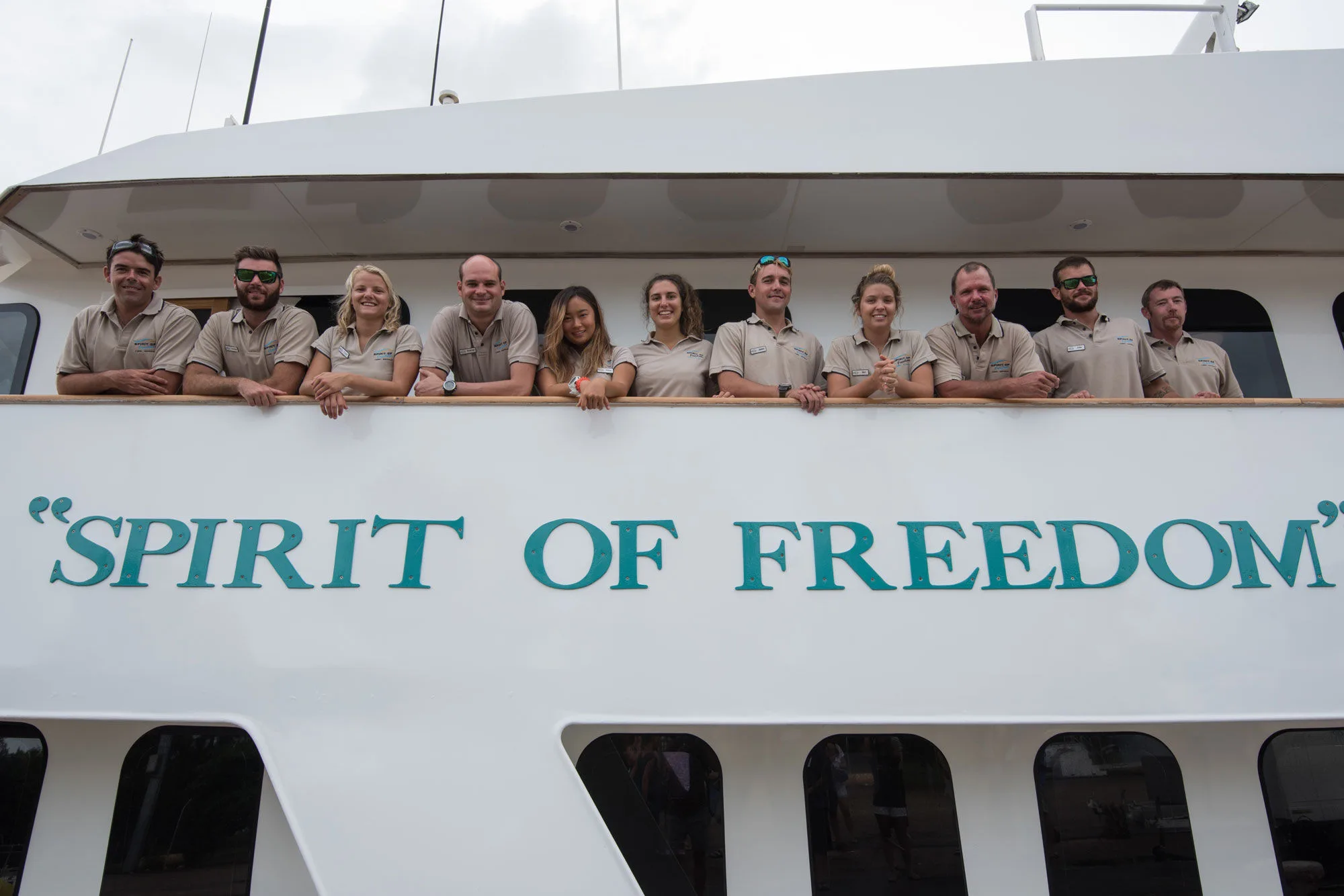 The crew of Spirit of Freedom along the rail above the vessel's name
