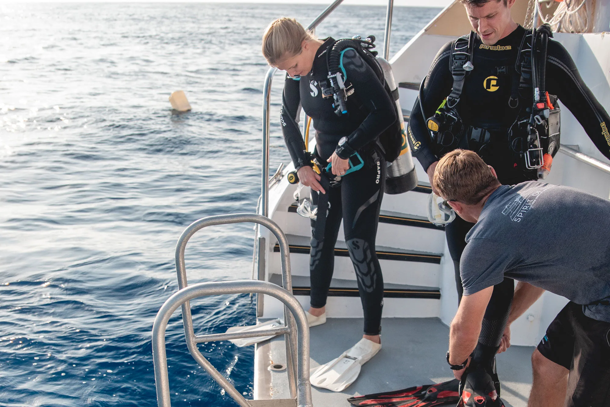 A crew member helping a guest into fins on the dive steps