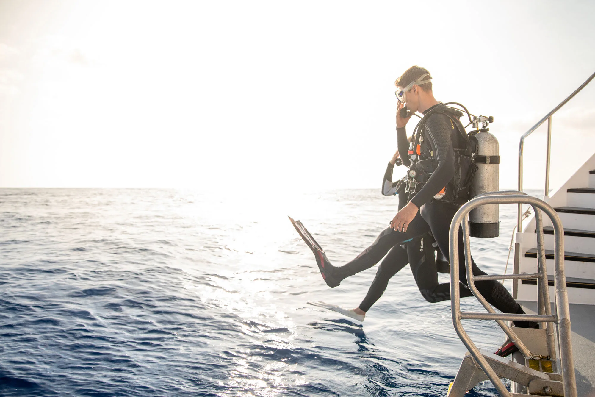 A diver giant-striding off the dive step into the sun