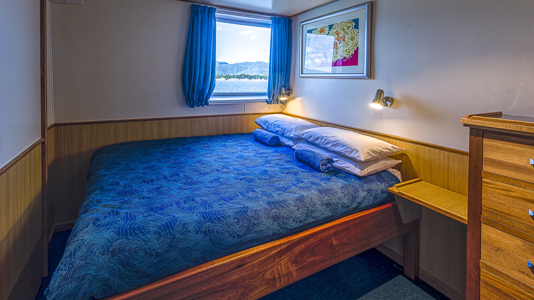 Premium cabin — blue bedspread, timber panelling and reading lights