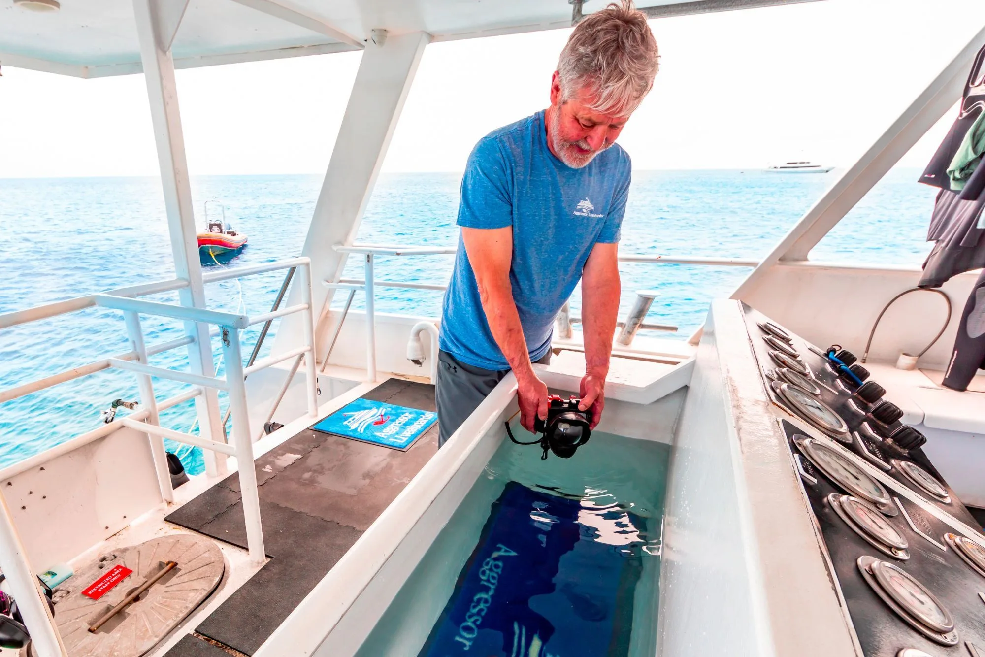 Crew member lowering a camera into the rinse tank on the dive deck