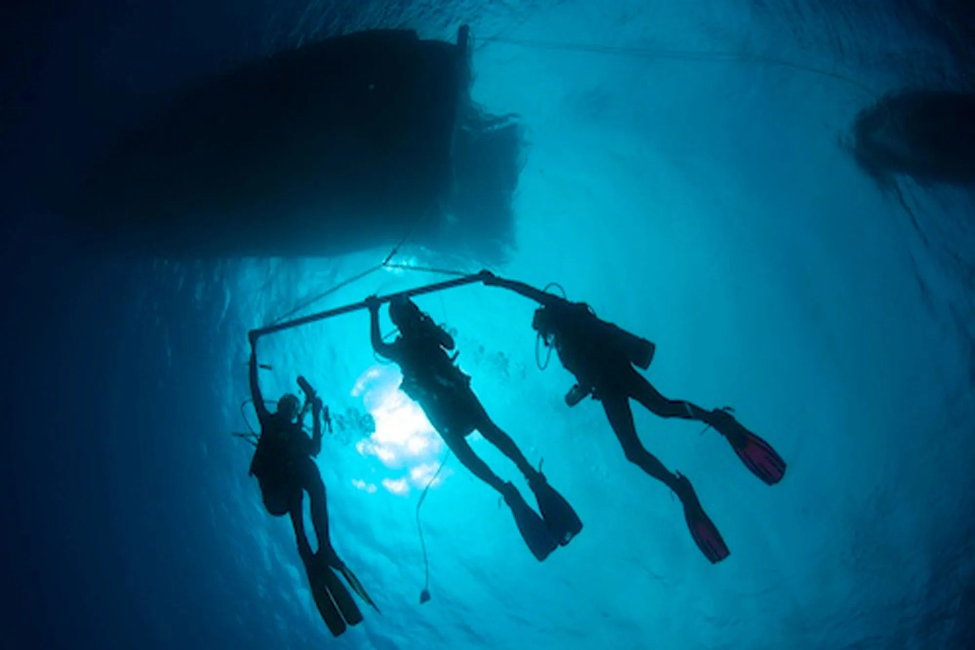 Divers on a safety stop silhouetted beneath the yacht
